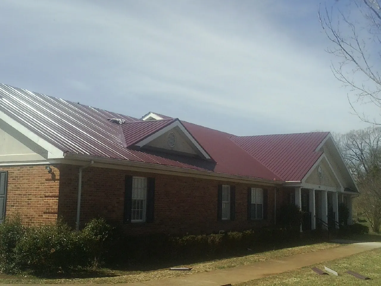 Red metal roof with gabled entries on a long brick building, from a Hail Damage Roof Repair job in Crossnore