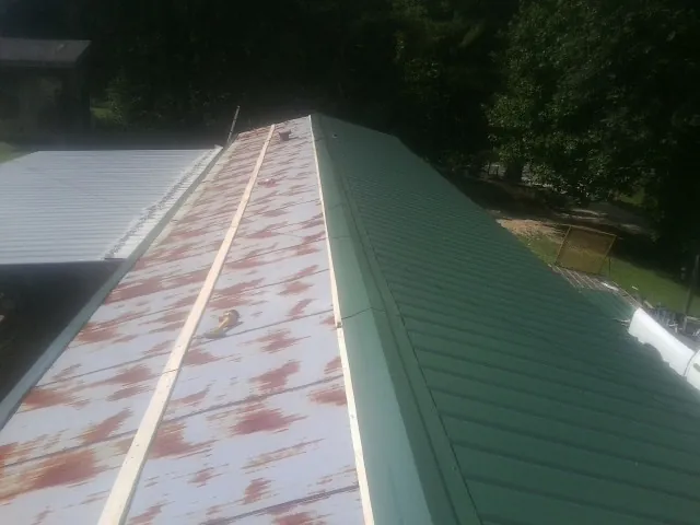 Old rusted panels beside newly installed green metal roofing — Wind Damage Roof Repair by Roofing Brothers in Crossnore