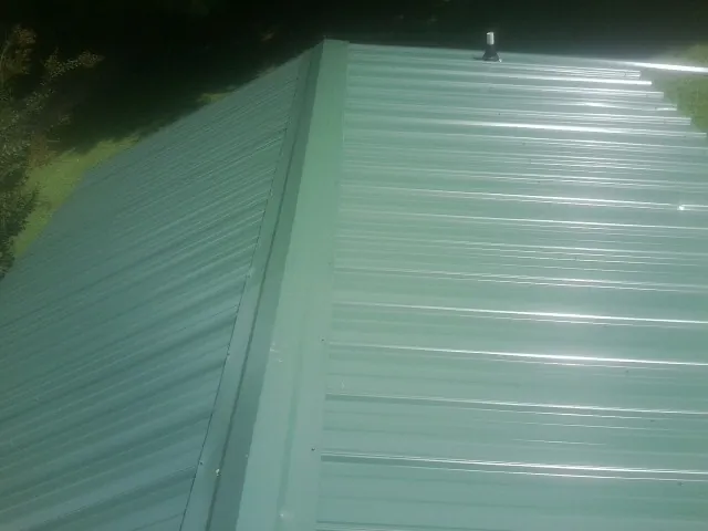 New green metal panels meeting at the ridge of a roof — Flat Roof Repair work by our crew in Crossnore