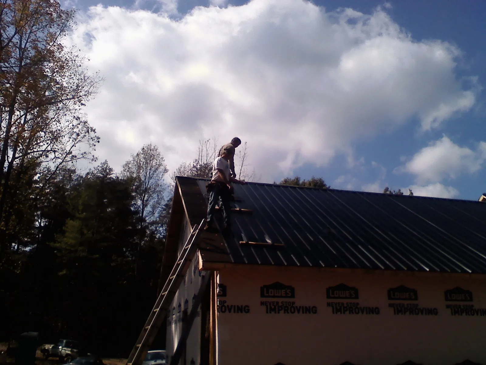 Roofer fastening dark metal panels high against a cloudy sky, from a Roof Inspection job in Crossnore