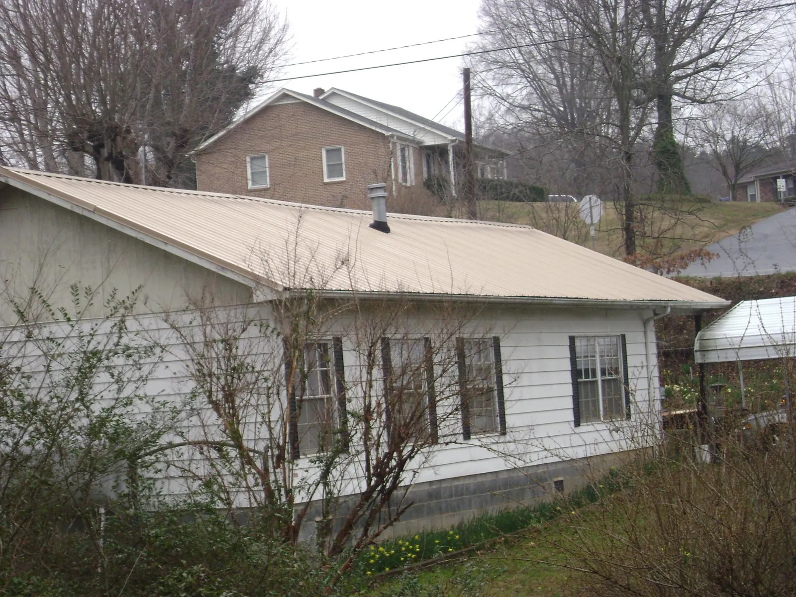 Tan metal roof on a white sided house set into a hillside — Commercial Roofing by Roofing Brothers in Crossnore