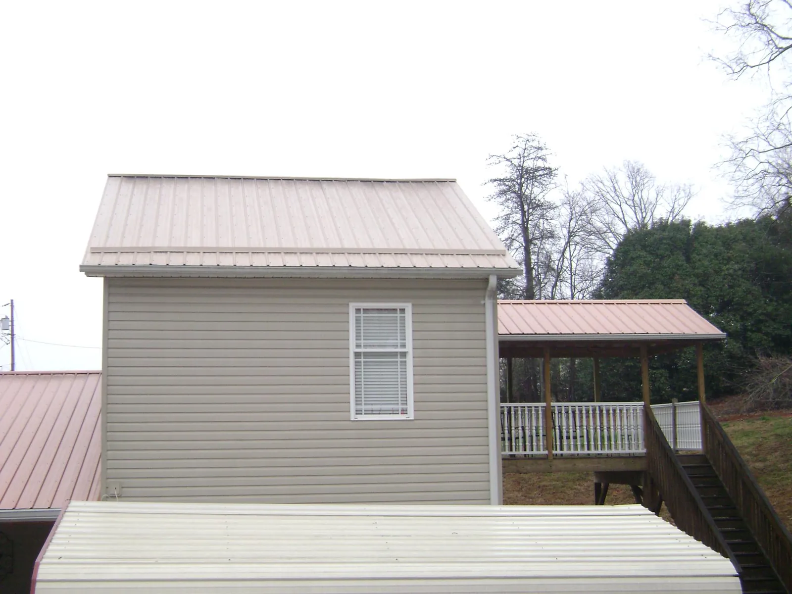 Tan metal roofs on a two story addition and attached porch, from a Roof Replacement job in Crossnore